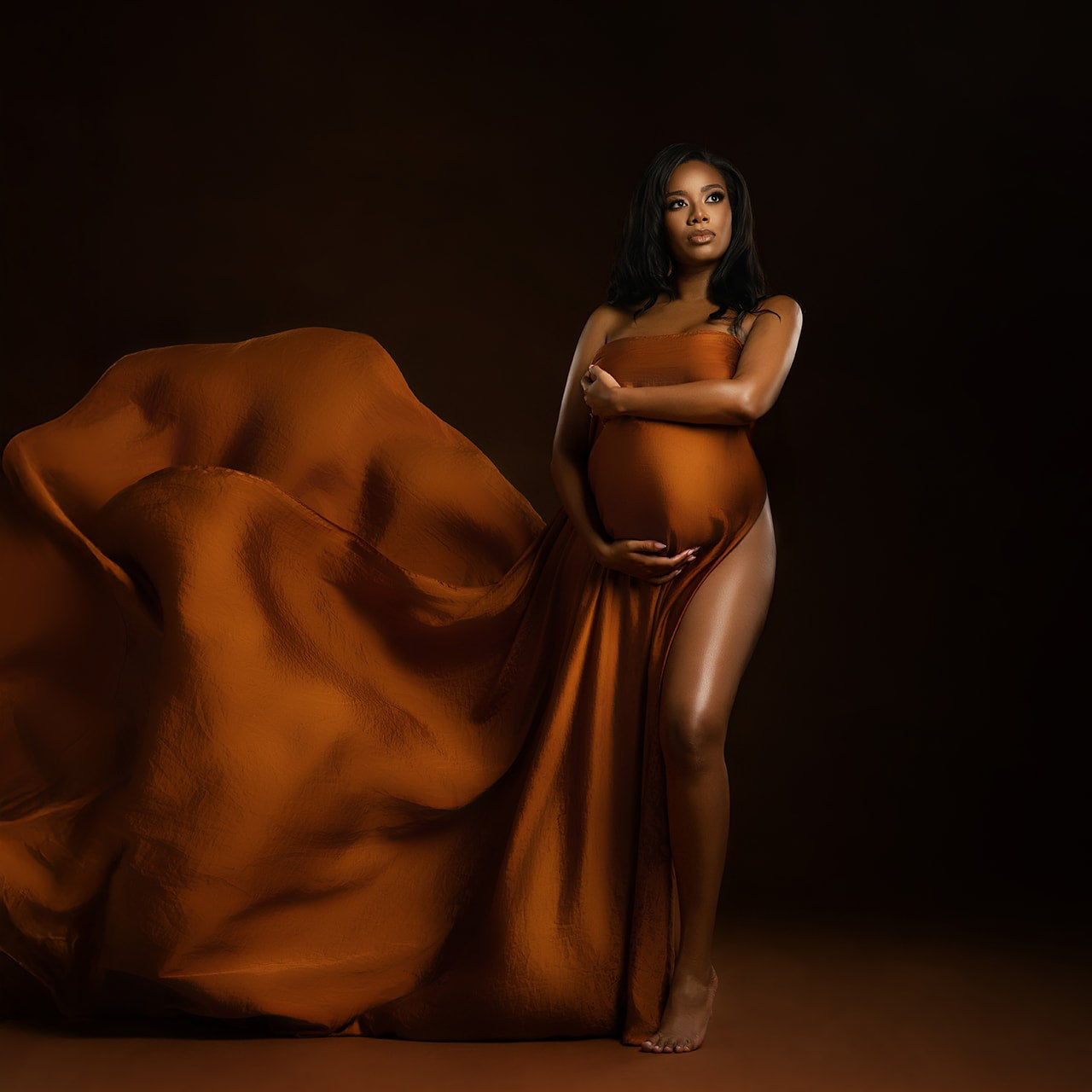Pregnant woman in an orange gown against a dark background Houston