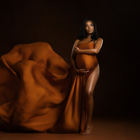 Pregnant woman in an orange gown against a dark background Houston